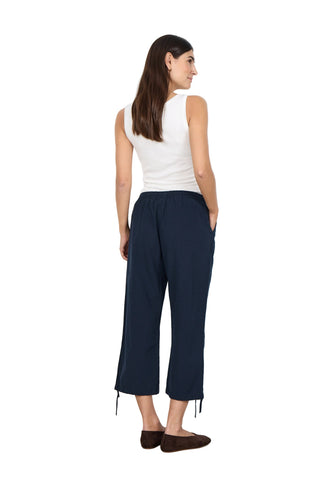 Woman wearing a white sleeveless top and navy blue pants against a white background
