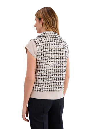 Woman wearing a houndstooth patterned vest over a beige top on a light gray background