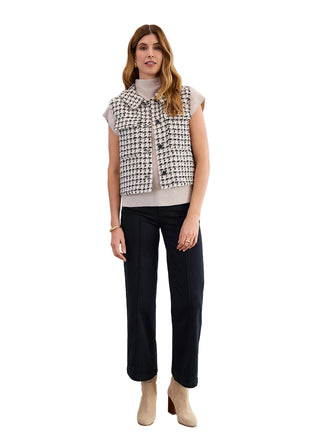 Woman wearing a patterned sleeveless top, black pants, and beige boots against a white background
