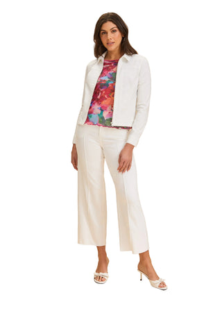 Woman wearing a white jacket, floral top, and white pants on a beige background