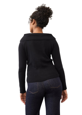 A woman viewed from the back wearing a black long-sleeve knit top with a wide collar and dark blue jeans, standing against a plain light background.