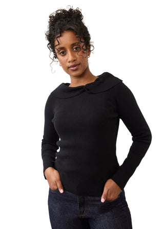 A woman modeling a black long-sleeve knit top with a wide collar and button detail at the neckline, paired with dark blue jeans against a plain light gray background.