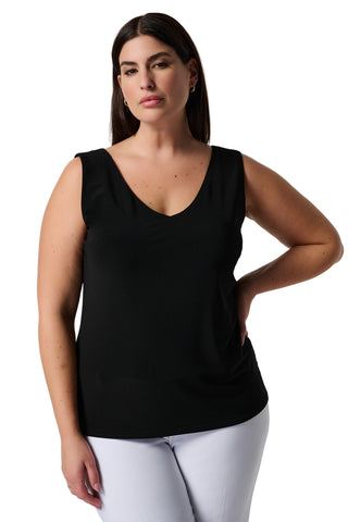 Woman wearing a black sleeveless top and white pants on a plain background
