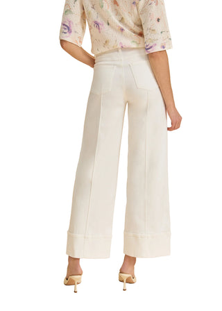 Person wearing a floral blouse and white wide-leg pants on a beige background