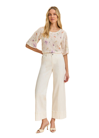 Woman wearing a floral blouse and white pants on a beige background