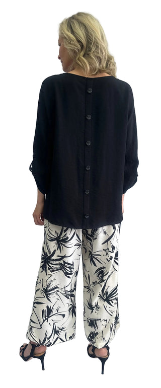 Woman wearing a black cardigan and white pants with black patterns against a white background