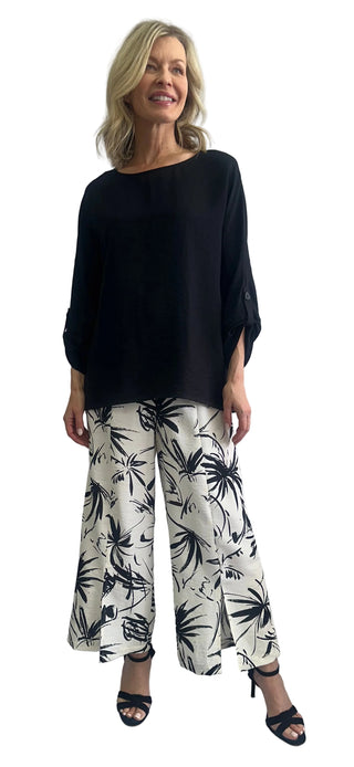 Woman wearing a black top and white pants with black patterns against a white background