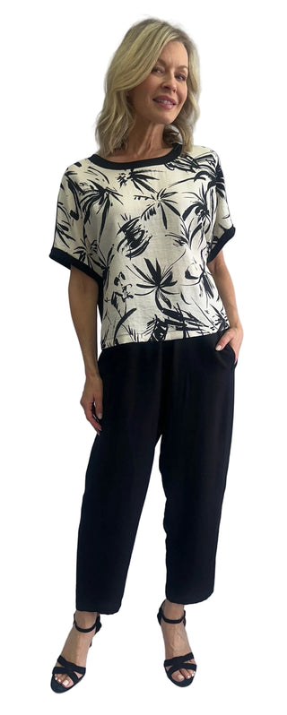 Woman wearing a patterned top and black pants against a white background