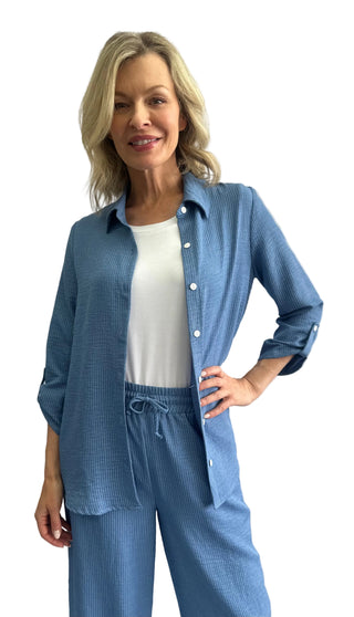 Woman wearing a blue textured shirt and pants set against a white background