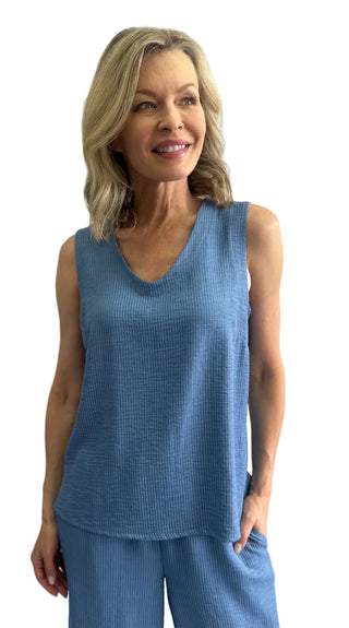 Woman wearing a blue sleeveless top and pants against a white background