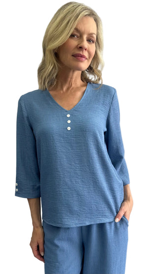 Woman wearing a blue textured top and pants against a white background