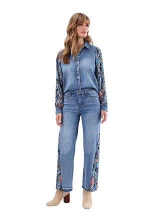 Woman wearing a denim shirt and jeans with floral sleeves against a white background