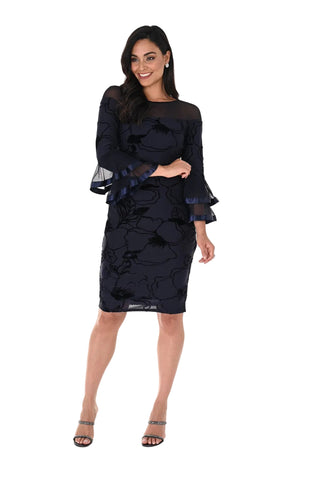 A woman modeling a black floral lace midi dress with sheer long sleeves, ruffled cuffs, and a peplum waist, paired with black strappy heels, against a plain white studio background.
