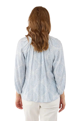 Woman wearing a light blue patterned blouse and white pants on a white background