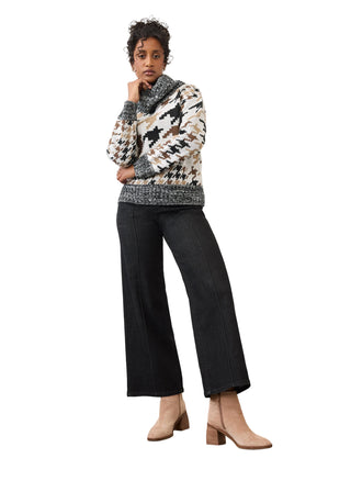 A woman models a patterned knit sweater with a cowl neck, paired with wide-leg black pants and beige ankle boots, standing against a plain studio background.