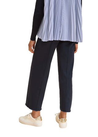 Person wearing navy pants with a black top and white sneakers on a beige background