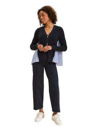 Woman wearing a navy cardigan over a striped shirt with navy pants on a beige background