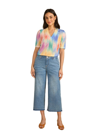 Woman wearing a colorful tie-dye shirt and blue jeans on a beige background