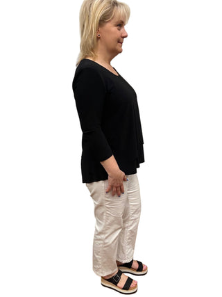 Woman wearing a black top and white pants standing in a fitting room.
