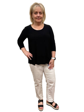 Woman wearing a black top and white pants standing in front of a mirror.