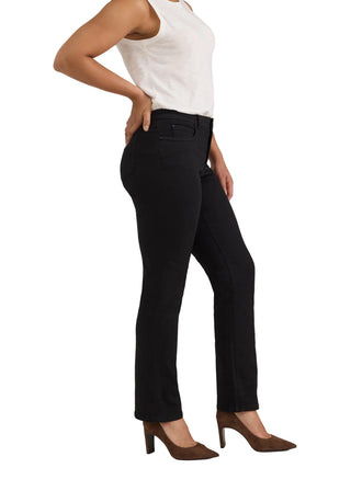 A model wearing black high-waisted straight-leg jeans, styled with a white sleeveless top and brown pointed-toe heels, shown from the waist down against a light gray studio background.