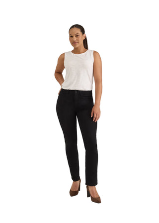 A woman modeling black skinny jeans with a white sleeveless top and brown heels, standing against a light gray studio background.