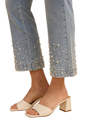 Light blue jeans with pearl embellishments and white sandals on a beige background