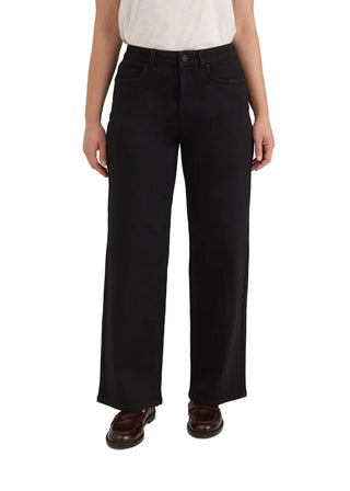 A model wearing black wide-leg cropped pants, styled with a white top and dark brown leather loafers, photographed against a neutral light gray studio background.