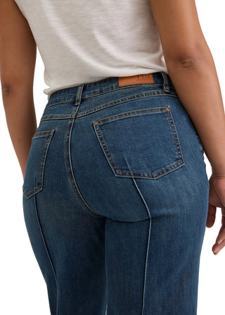 Close-up back view of a person wearing blue denim jeans with a white top, showing the back pockets and waistband.