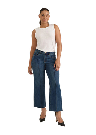 A woman modeling a pair of dark blue wide-leg cropped jeans with a white sleeveless top and black heels, standing against a light gray studio background.