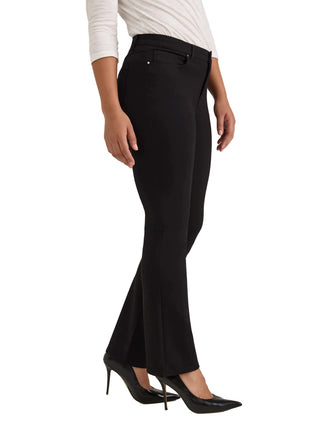 A model wearing black flared trousers with a front slit, paired with a white long-sleeve top and black pointed-toe heels, shown from the waist down against a light gray studio background.
