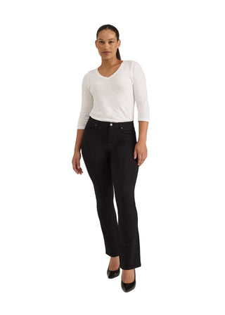 A woman modeling black high-waisted straight-leg jeans with a white long-sleeve top and black pointed-toe heels, standing against a light gray studio background.