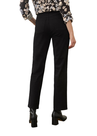 A model shown from the back wearing black wide-leg cropped trousers, a black floral long-sleeve blouse, and black ankle boots, standing on a concrete floor against a light beige wall.