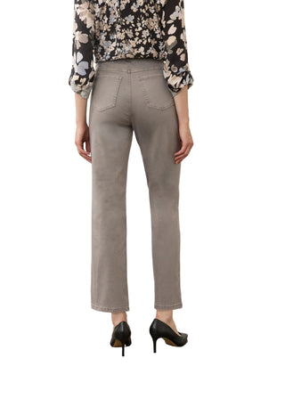 A person shown from the back wearing light gray cropped straight-leg jeans, a black floral blouse, and black heels, standing against a plain off-white wall and concrete floor.