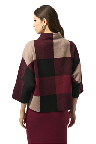 Woman wearing a checkered poncho with burgundy, beige, and black pattern on a white background