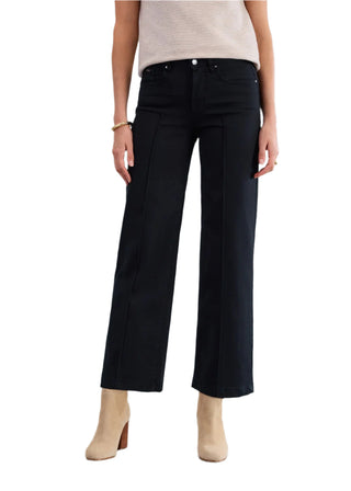 Person wearing black wide-leg jeans and beige shoes on a plain background