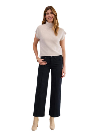 Woman wearing a beige turtleneck and black pants against a white background