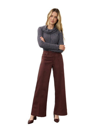 A woman modeling a dark gray cowl-neck knit sweater and dark brown wide-leg trousers, standing with arms crossed against a neutral studio backdrop.