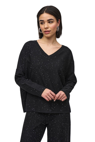 Woman wearing a black long-sleeve top and pants with small speckles on a white background