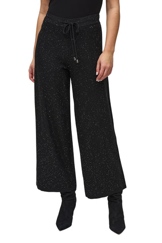 Person wearing black speckled wide-leg pants on a white background