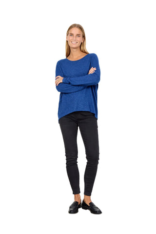 Woman wearing a blue sweater and black pants standing against a white background
