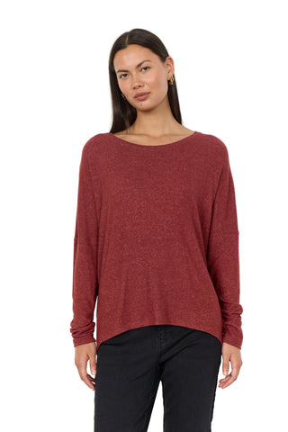 A woman modeling a long-sleeve, boat-neck knit sweater in a heathered rust red color, paired with black pants, against a plain white studio background.