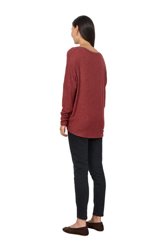 A woman shown from the back wearing a heathered rust-red long-sleeve top, black skinny pants, and brown flats, standing against a plain white wall.
