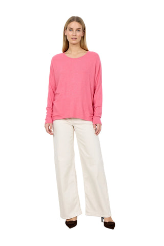 Woman wearing a pink sweater and white pants against a white background