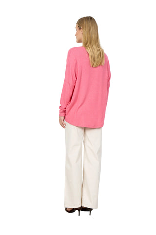Woman wearing a pink sweater and white pants against a white background