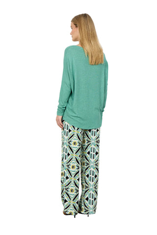 Woman wearing a green long-sleeve top and patterned pants against a white background