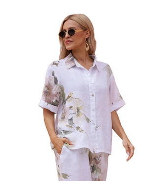 Woman wearing a floral shirt and pants standing in front of a peach-colored building.