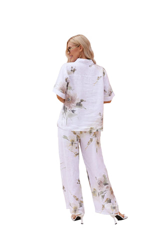 Woman in a white floral outfit standing in front of architectural columns.