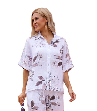 Woman wearing a floral outfit standing against a beige wall.