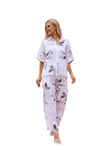Woman in a white floral outfit standing in front of a desert-like background with architectural columns.
